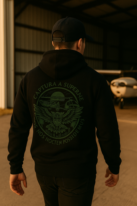 Person wearing a black hoodie with a logo and text, walking in an industrial setting.