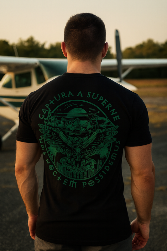 Man wearing a black t-shirt with green graphic and text, standing in front of an airplane.